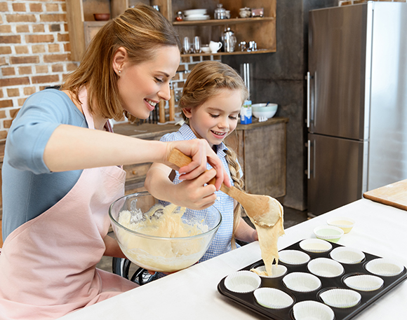 Kvinne og barn legger deig i muffinsformer.Foto