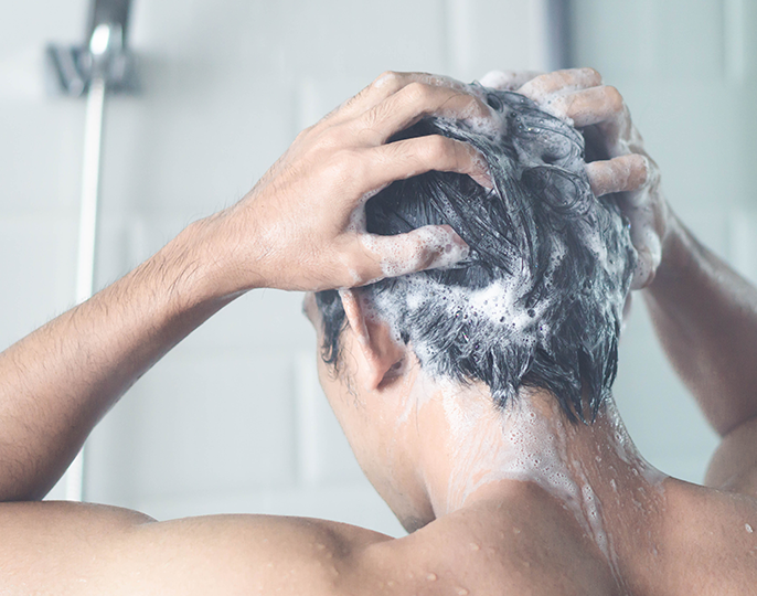 Mann står i dusjen og masserer sjampo inn i håret.Foto