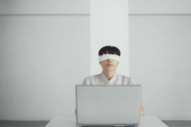 Bilde av mann med bind for øynene som sitter foran en PC.FotoFoto