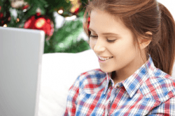 Kvinne ved laptop med juletre i bakgrunnen.Foto