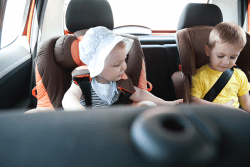 Liten jente og gutt sitter i barnesete i bil.Foto