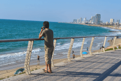 Mann snakker i mobil ved stranda.Foto