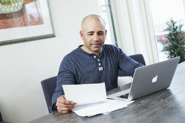 Mann med regning i hånden foran en laptop.Foto