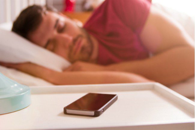 Sovende mann med mobiltelefon på nattbordet.Foto