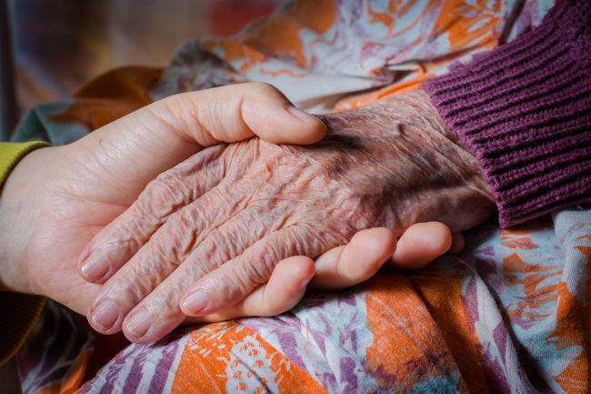 Ung persons hånd holder en eldre persons hånd.Foto