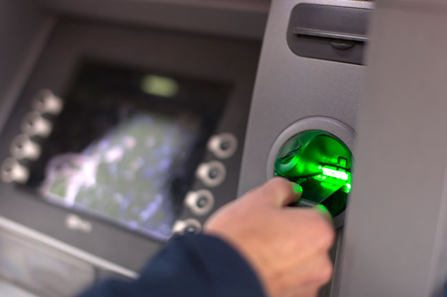 Nærbilde av hånd som putter bankkort inn i minibank.Foto