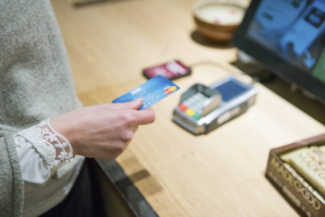 Nærbilde av hånd med bankkort ved bankterminal.Foto