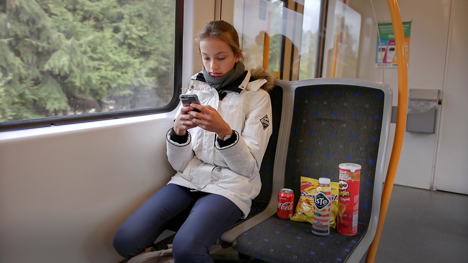 Ung jente sitter på bussen med mobil i hånda.FotoFoto