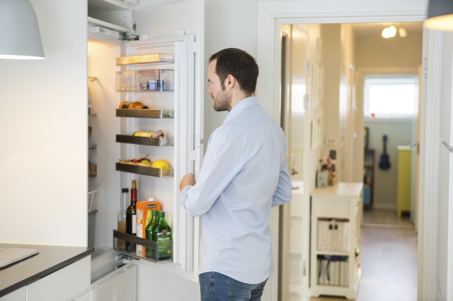 Mann som står med åpen kjøleskapsdør.Foto