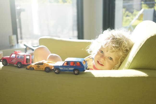 Bilde av et lite barn som leker i en sofa med sollys fra vinduet.Foto