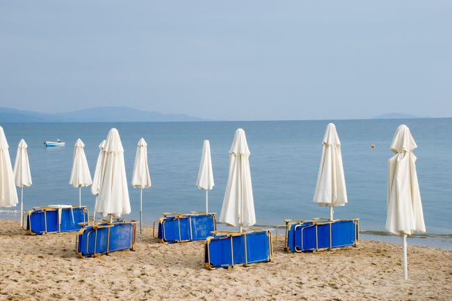 Bilde av en sandstrand med solsenger og nedslåtte parasoller.Foto
