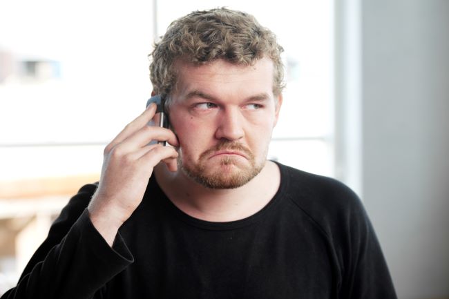 Mann holder mobiltelefon til øret og ser veldig sur ut.foto