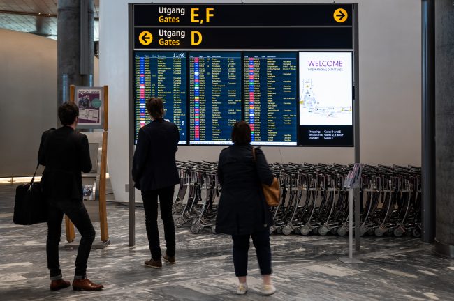 Flyreisende står ved en avgangstavle og ser på Kansellerte reiser. Foto