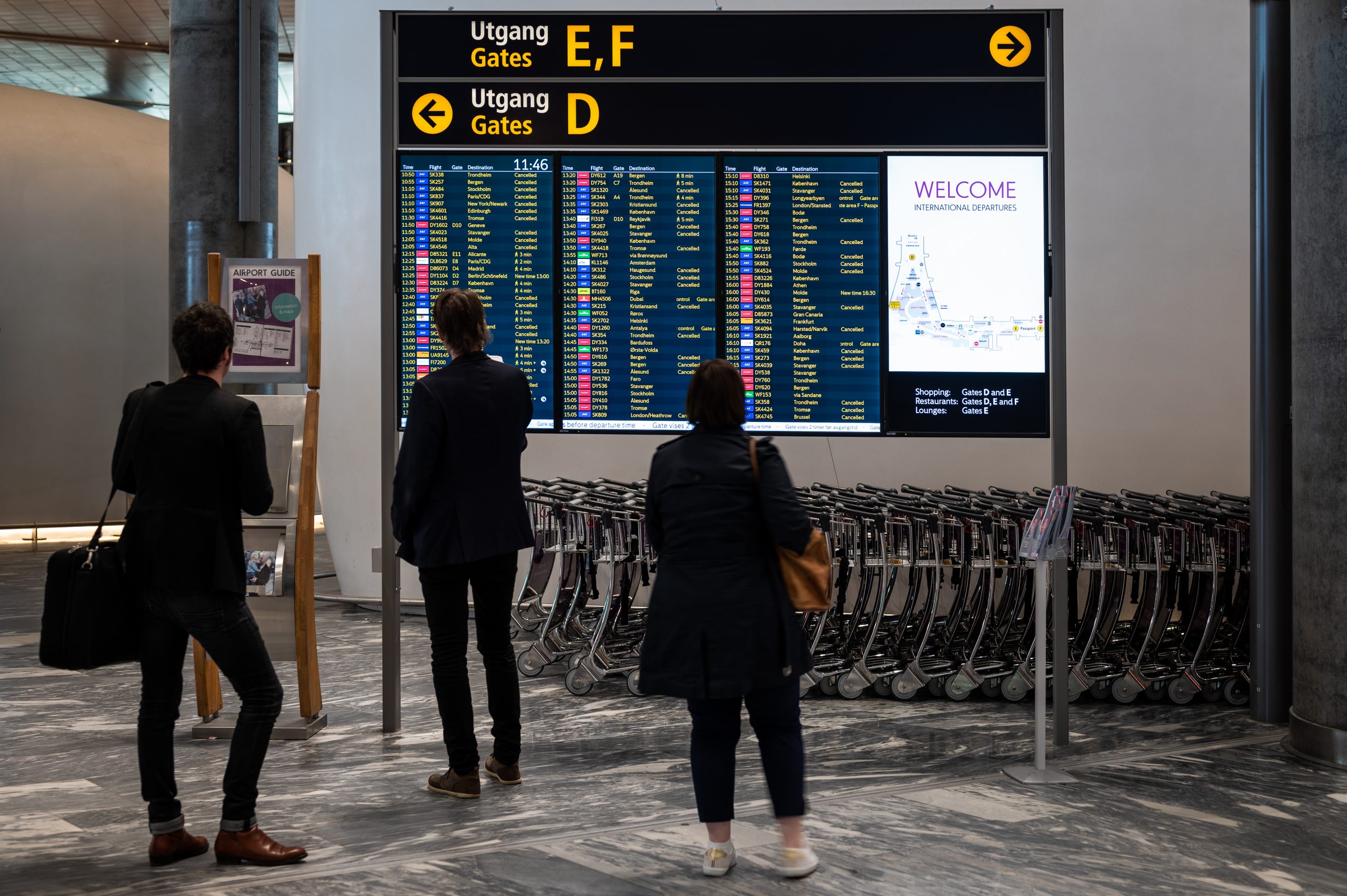 Flyreisende står ved en avgangstavle og ser på Kansellerte reiser. Foto
