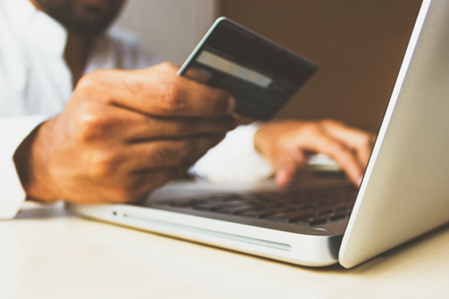 Illustrasjonsfoto av en person som betaler med kredittkort foran en bærbar datamaskin.foto