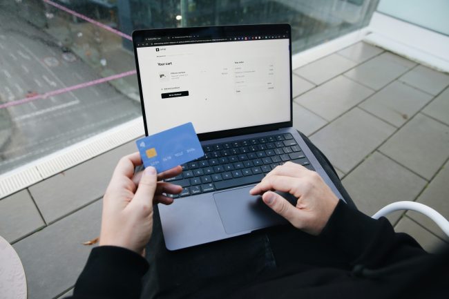 Hender som holder i et kredittkort foran en pc.foto