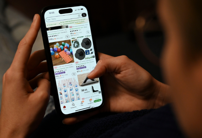 Hender som scroller på en mobilskjerm som viser nettbutikken Temu.foto